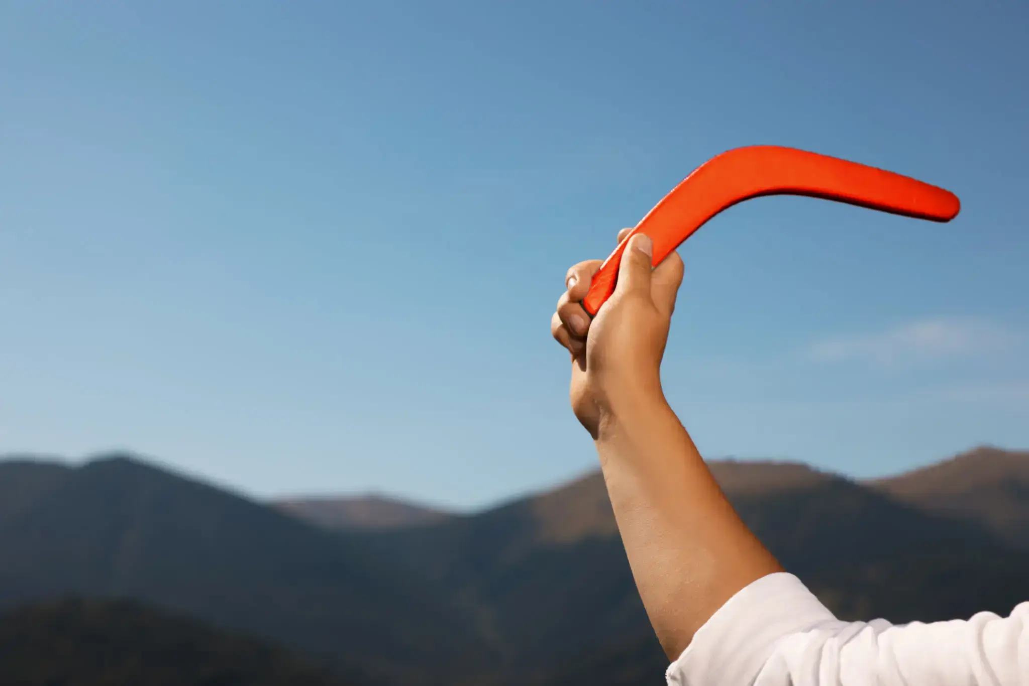 Una mano solleva un boomerang rosso contro il cielo e le montagne