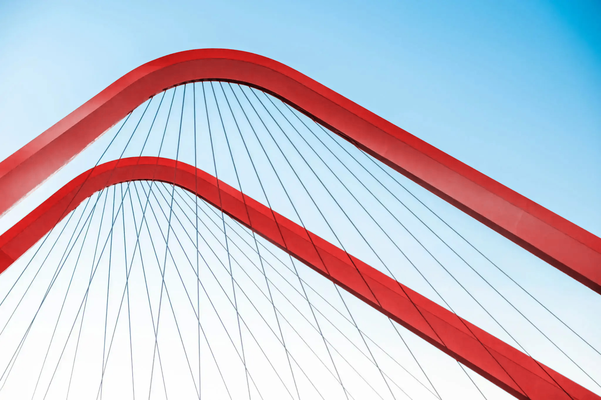 Red arch of a cable-stayed bridge against the sky